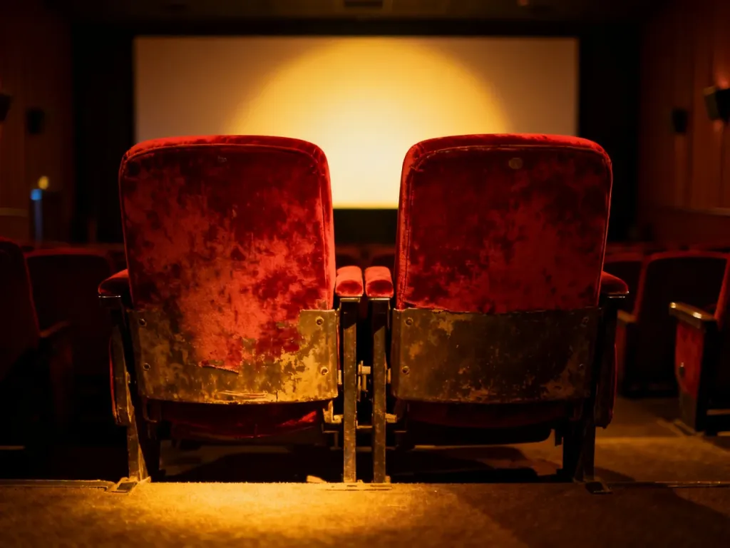 Dwa puste, aksamitne fotele w kinie oświetlone ciepłym światłem, budujące nastrojowy i romantyczny klimat filmu.